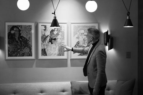 Portrett av Wiljelm Hartwig som peker mot kunst på hotellet sitt