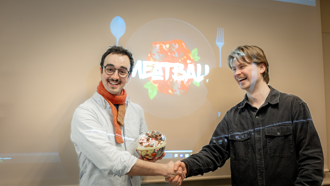 Student mottar gratulasjoner under Norwegian Game Awards, med spillet «Meatball» vist på skjerm i bakgrunnen.