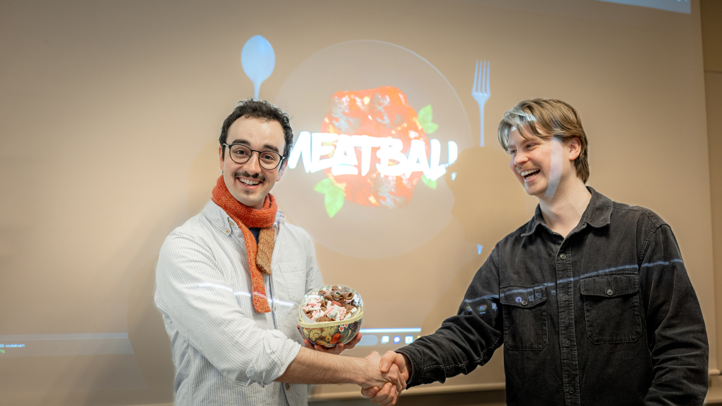 Student mottar gratulasjoner under Norwegian Game Awards, med spillet «Meatball» vist på skjerm i bakgrunnen.
