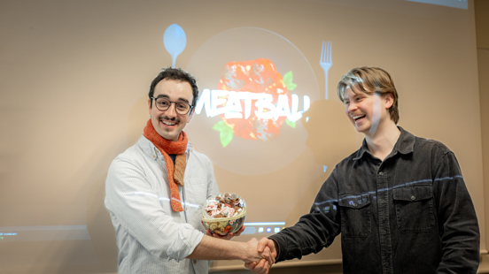Student mottar gratulasjoner under Norwegian Game Awards, med spillet «Meatball» vist på skjerm i bakgrunnen.