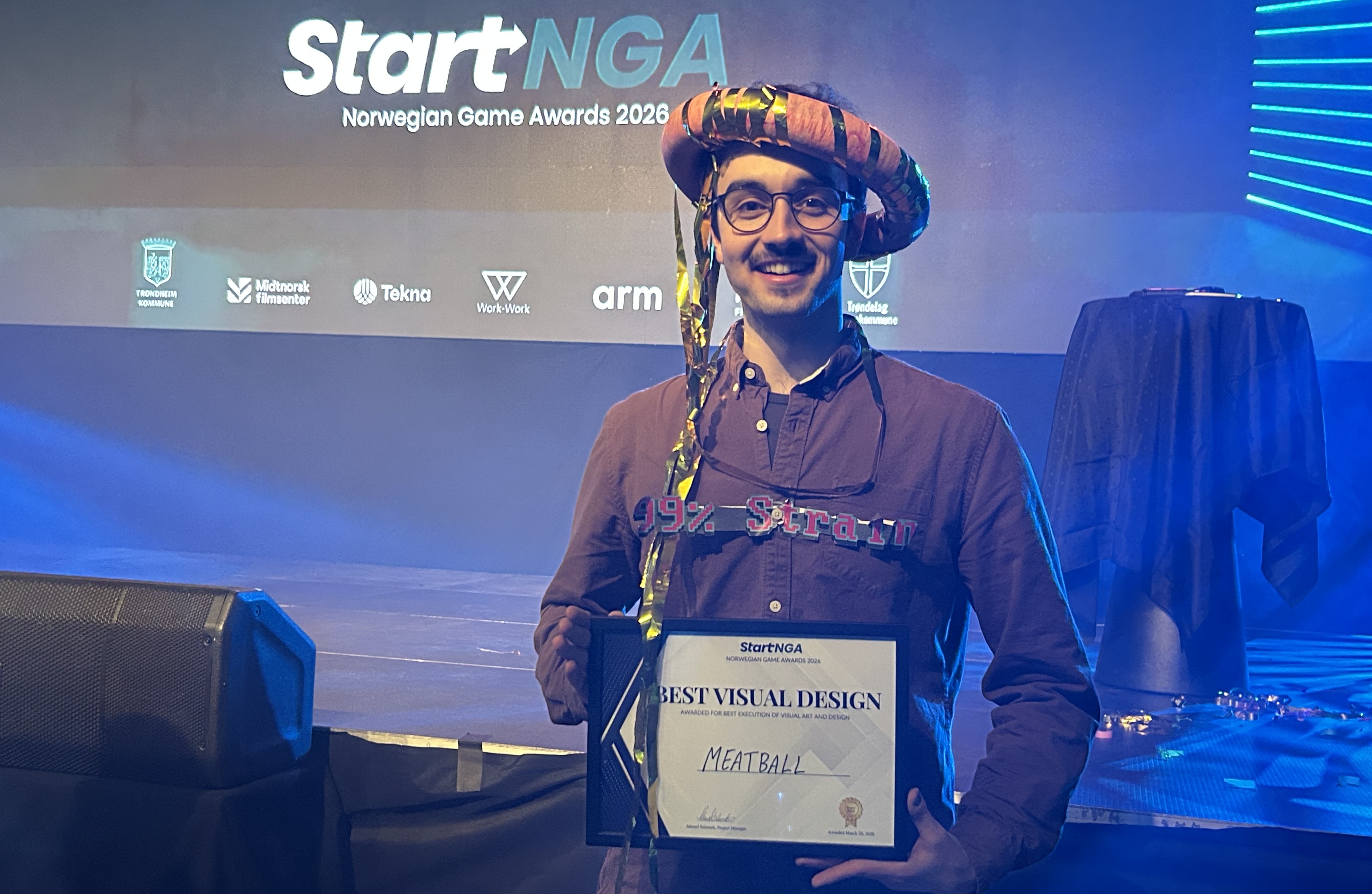 Student Shahin på en scene som holder diplom for Best Visual Design foran bakgrunn med StartNGA – Norwegian Game Awards.