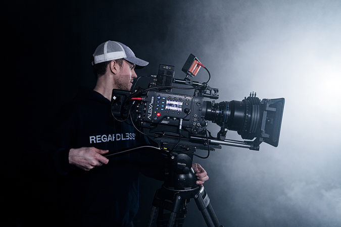 Student med stort filmkamera foran en sterk lyskilde.