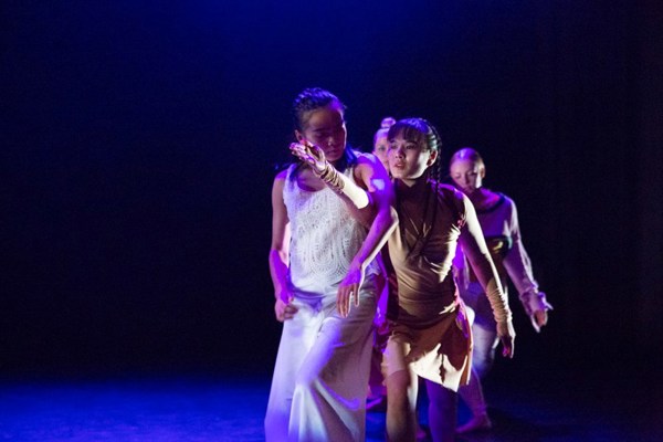 Foto av tre dansere som står på en rad, på en scene.