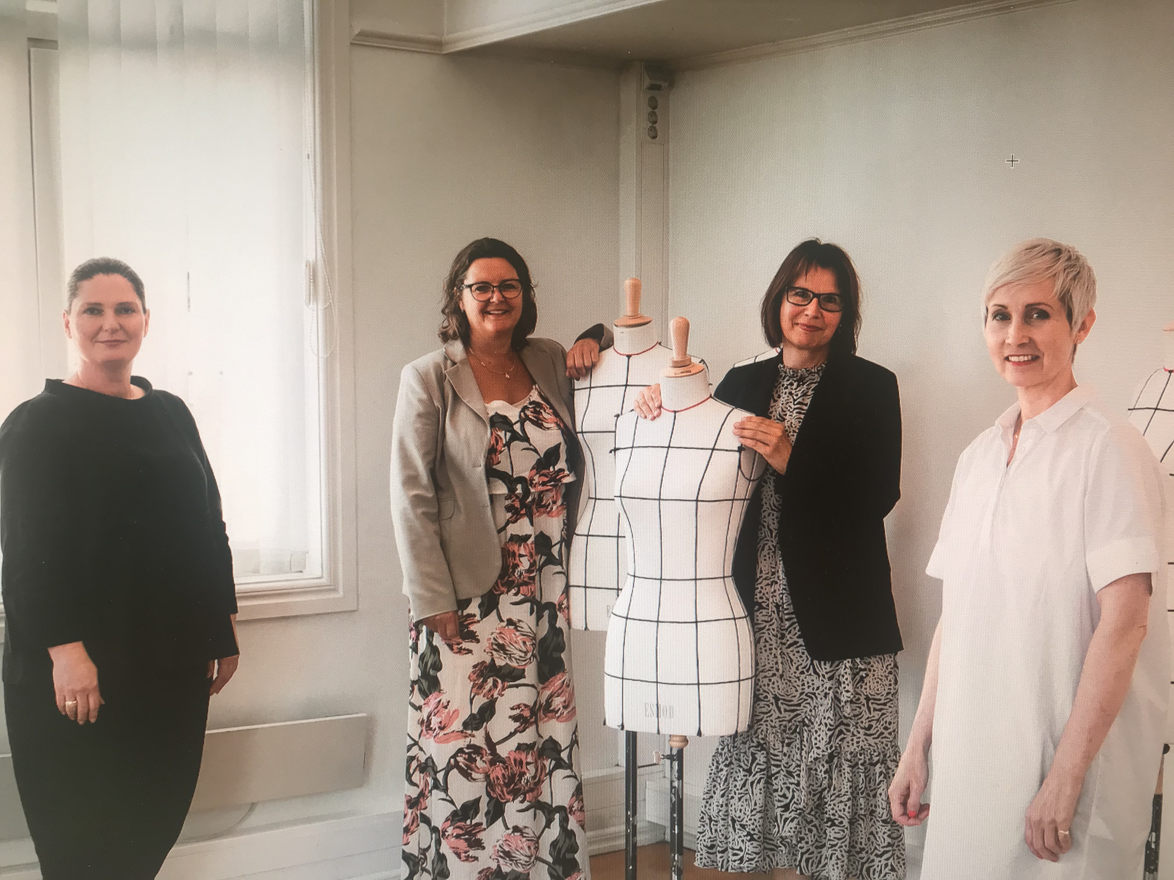 Bildet viser fire damer som står sammen med to skredderbyster og smiler.