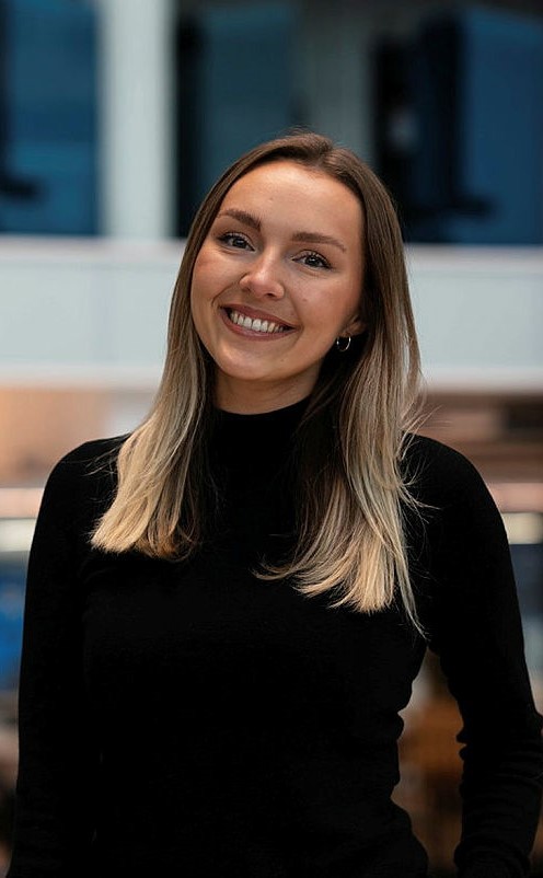 Foto av Amalie Trengereid, hun har på seg en mørk genser og smiler bredt. 