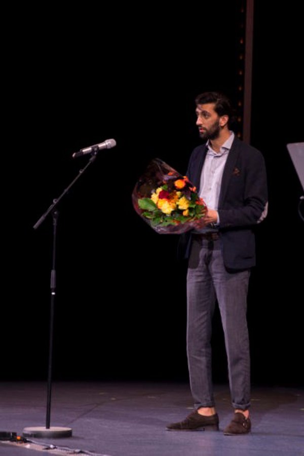Foto av student på scene med blomster i hånda.
