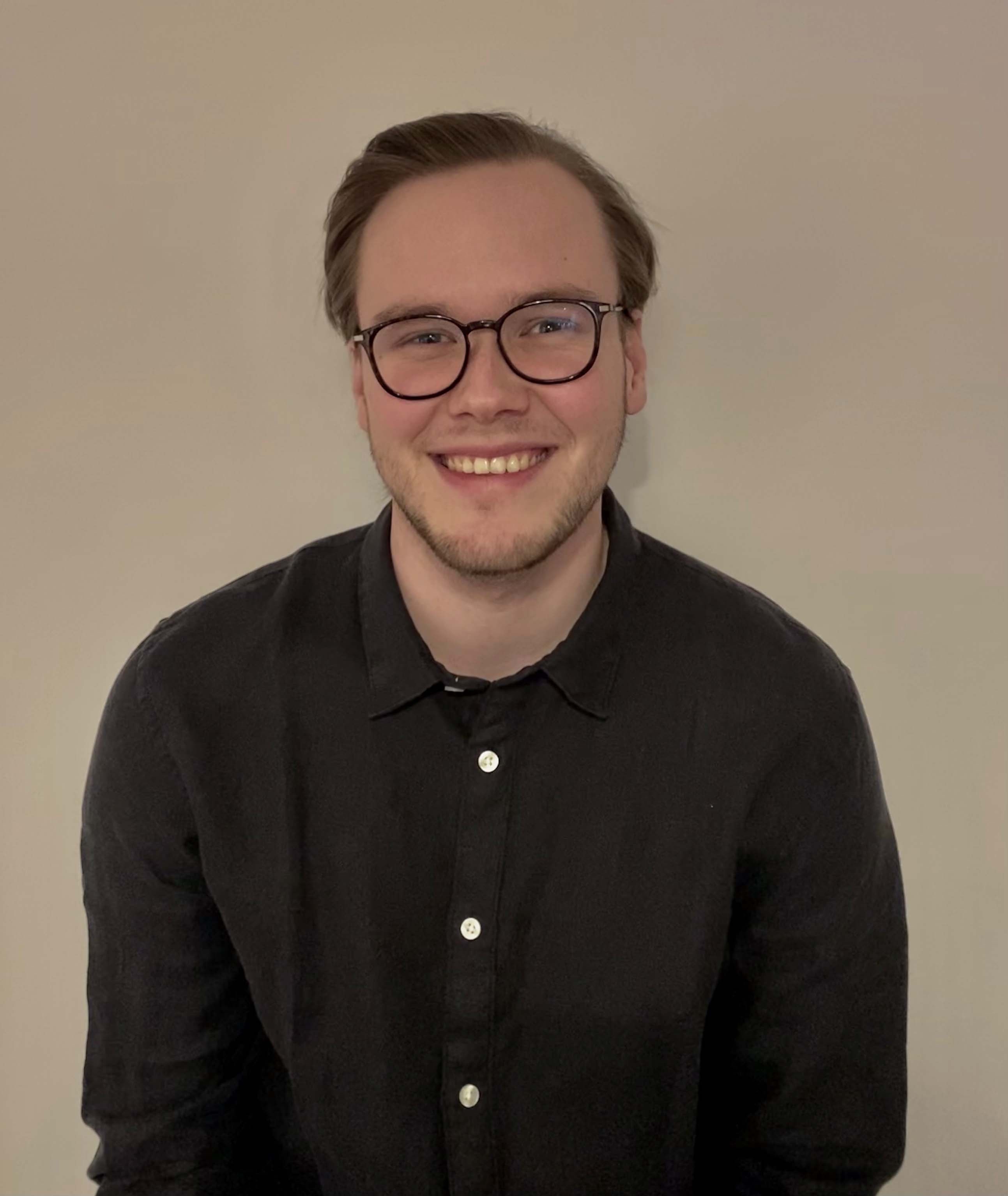 Elias Haugen smiler direkte mot kamera. Han har på briller og en sort skjorte. Foto.