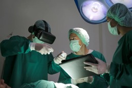 En lege med VR briller snakker med to kolleager under en operasjon
