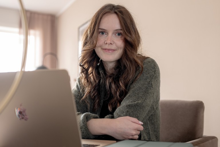 Nettstudent sitter bak bærbar laptop og ser inn i kamera