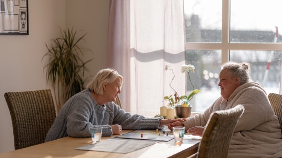 To personer sitter inne ved et spisebord i en samtale sammen