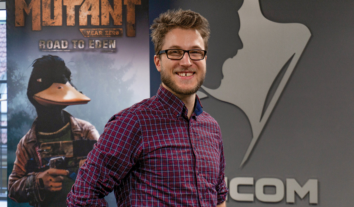 Rasmus Valand Fredriksen på jobb hos Funcom. Han har briller, skjegg og en rødrutete skjorte.