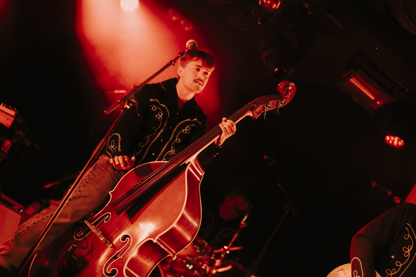 Musiker med western-skjorte spiller kontrabass i band på scene.