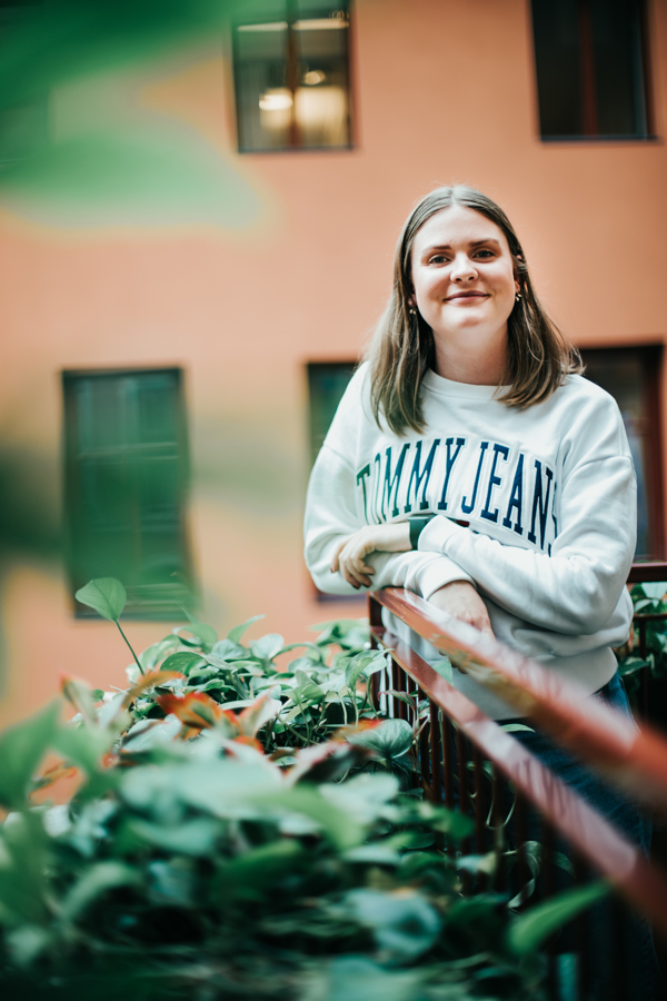 Masterstudent Maren Lindseth iført hvit genser lener seg på rekkverk med grønne planter.