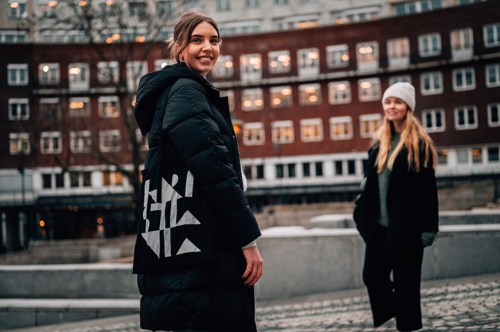 To kvinnelige studenter står ute på gaten. Begge er ikledd sorte vinterjakker, og den ene av dem har et Kristiania-nett over skulderen.