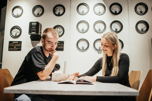 Foto av kvinnelig og mannlig student ved et bord som ser i en bok sammen.