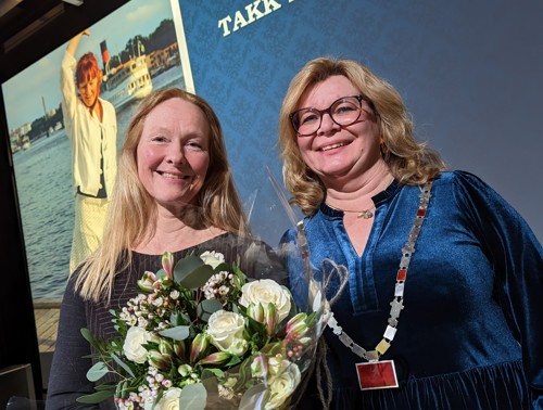 Hilde Rustad får blomster av rektor Trine Meza i etterkant av tiltredelsesforelesning. Bilde av Hilde Rustad i bakgrunnen.