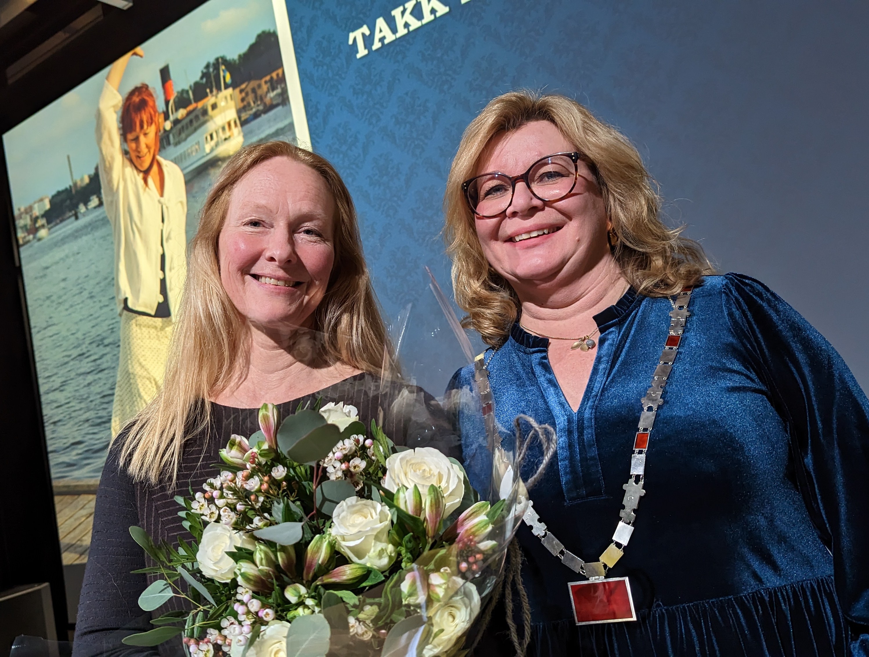 Hilde Rustad får blomster av rektor Trine Meza i etterkant av tiltredelsesforelesning. Bilde av Hilde Rustad i bakgrunnen.