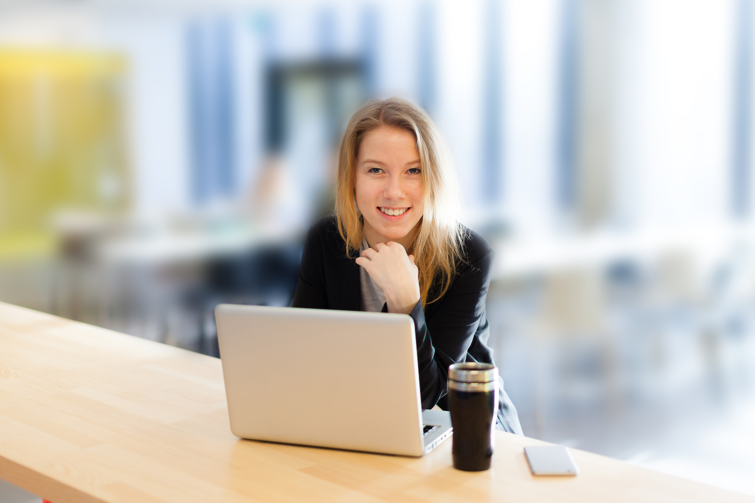 Foto av en kvinne med en pc og kaffekopp som ser i kamera og smiler.