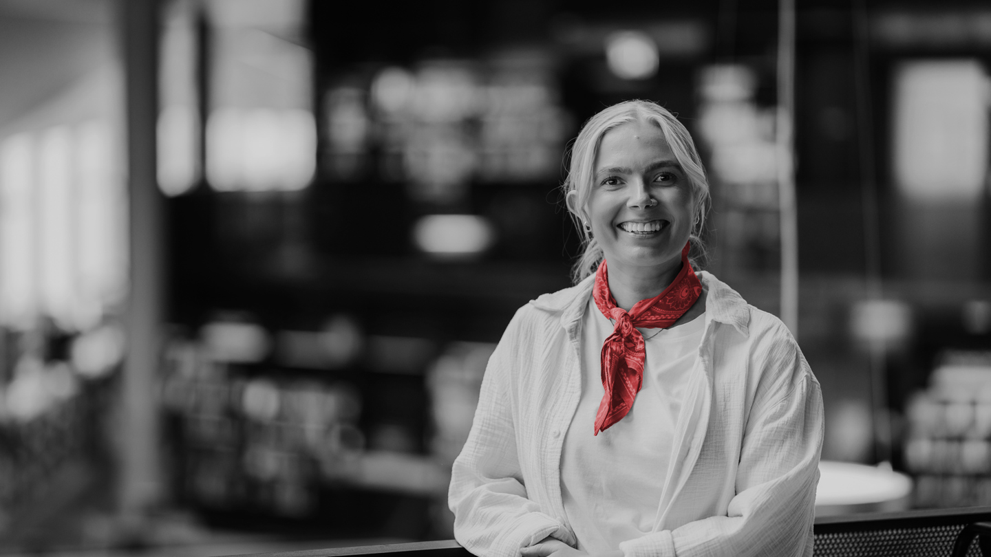 Kvinne i kontorlandskap ser mot kamera.