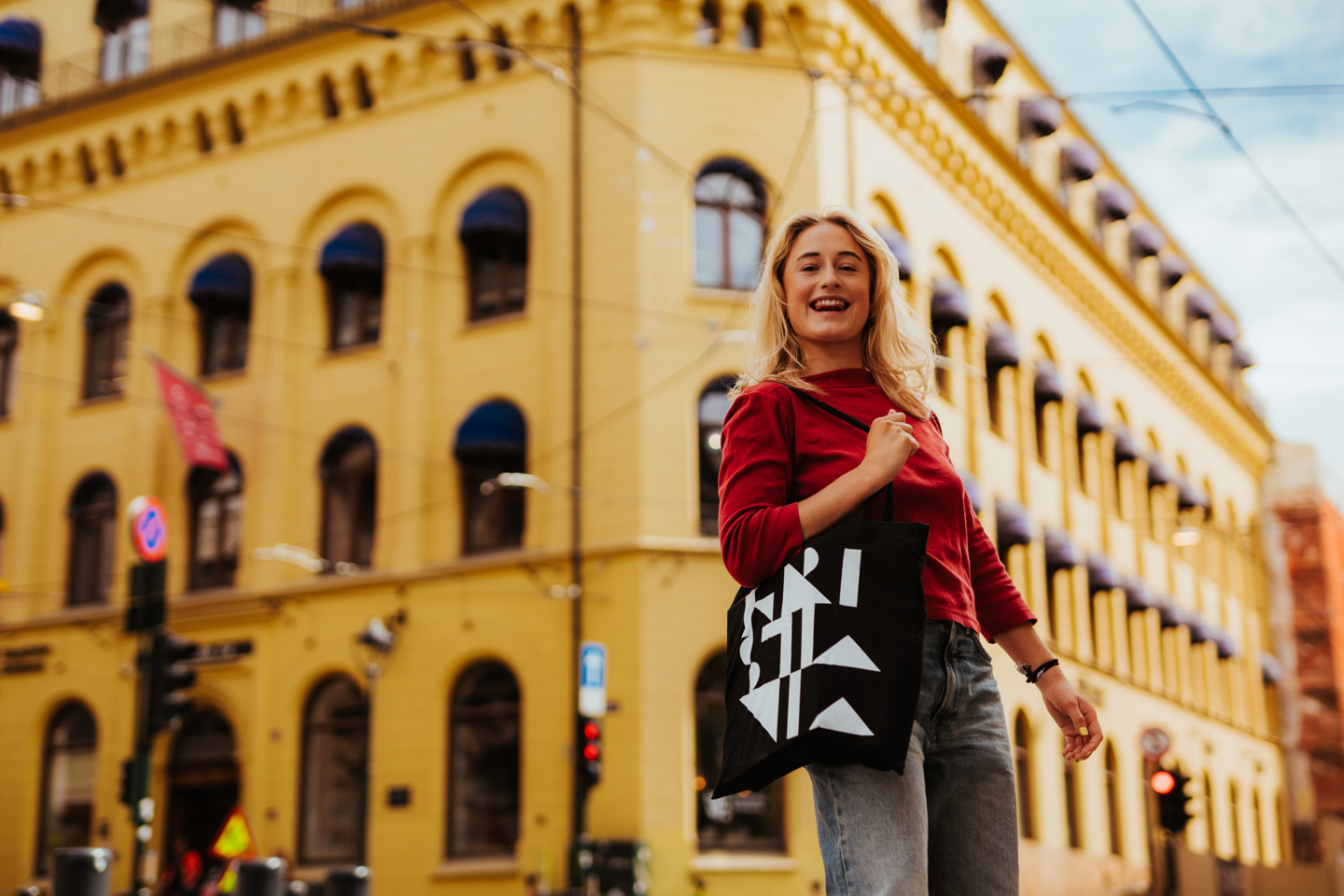 Student med Kristiania-veske foran campusbygg, bildelenke til studieoversikt.
