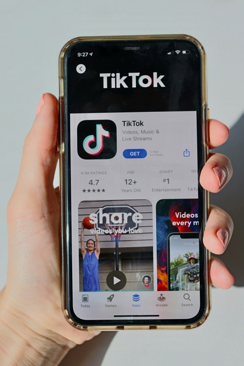 Hånd som holder mobiltelefon, som viser frem TikTok- appen i App Store på Iphone.