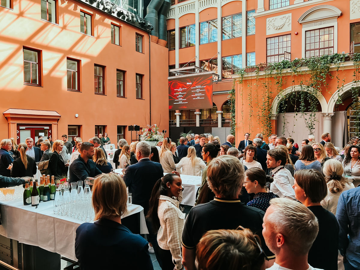 Oversiktsbilde av mange mennesker i et stort festlokale i en gammel bakgård med overbygget glasstak.