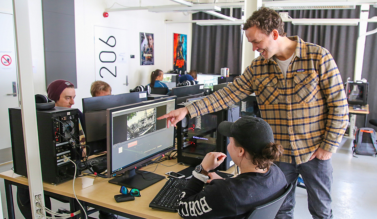 Hans Gunnar står og peker på en pc-skjerm og forklarer til en student.