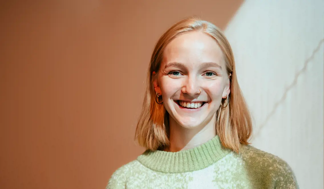 Kvinne med mellomlangt blondt hår og grønn strikket genser smiler