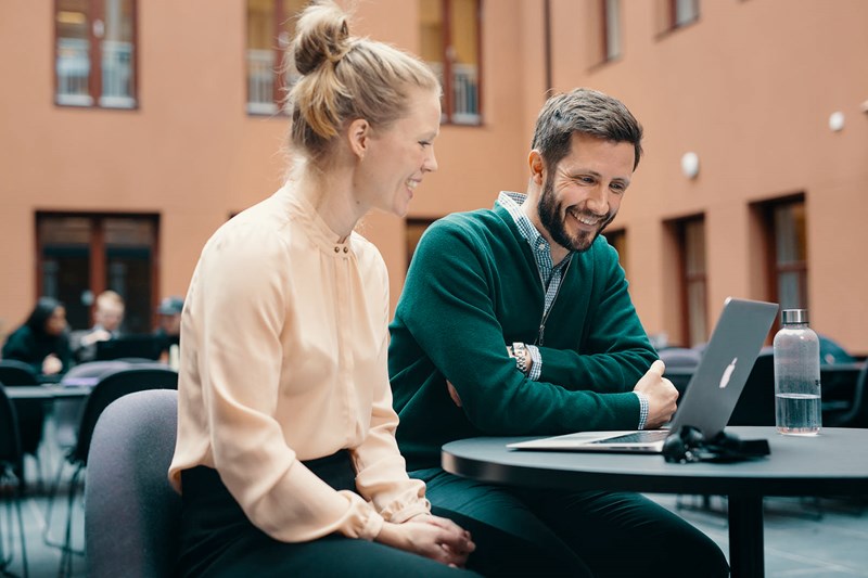 Foto av mann og kvinne som sitter sammen på et bord og ser på en laptop.