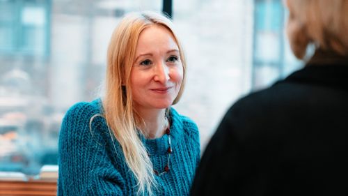 Kvinne sitter i samtale med en annen kvinne som har ryggen til.