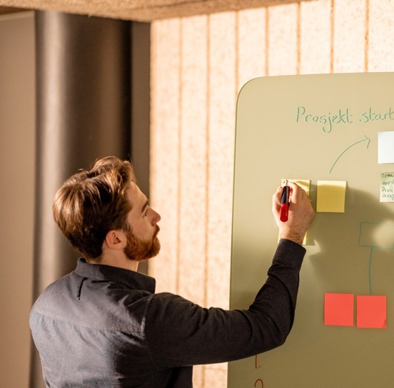 Person skriver på en post-it lapp til et prosjekt på en tavle. 