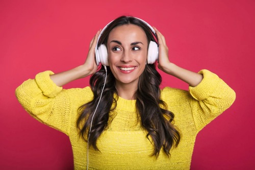 En kvinne står med hendene på hodetelefonene sine og ser til venstre for kameraet og smiler