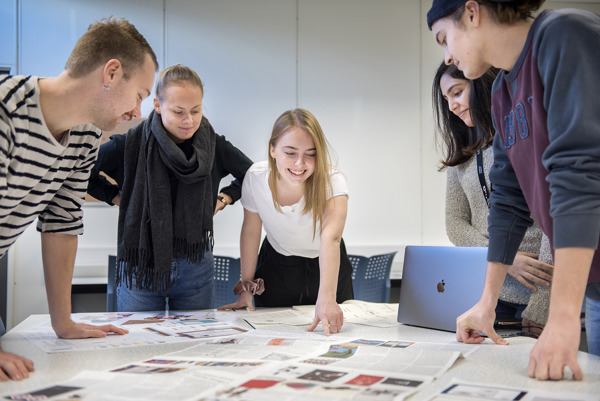 Studenter diskuterer skisser rundt et bord. Fagskolestudiet Grafisk Design ved Høyskolen Kristiania.