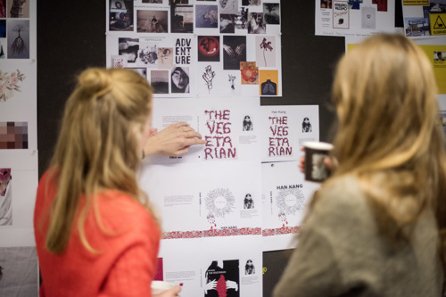 To studenter ser på grafiske arbeider på en vegg.