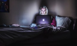 Woman sitting in her bed in the dark on her computer