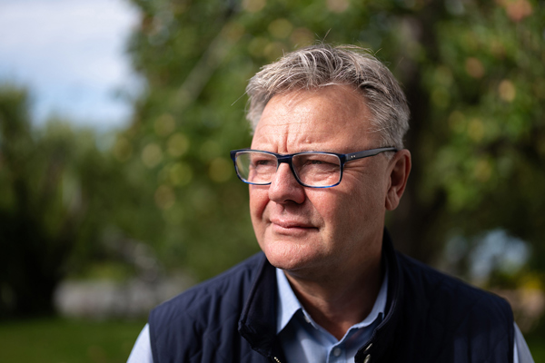 Bilde av Trond Adland, konsernsjef i Lund-gruppen. En person med briller ser tankefullt ut i det fjerne, med et uskarpt naturlig landskap i bakgrunnen.