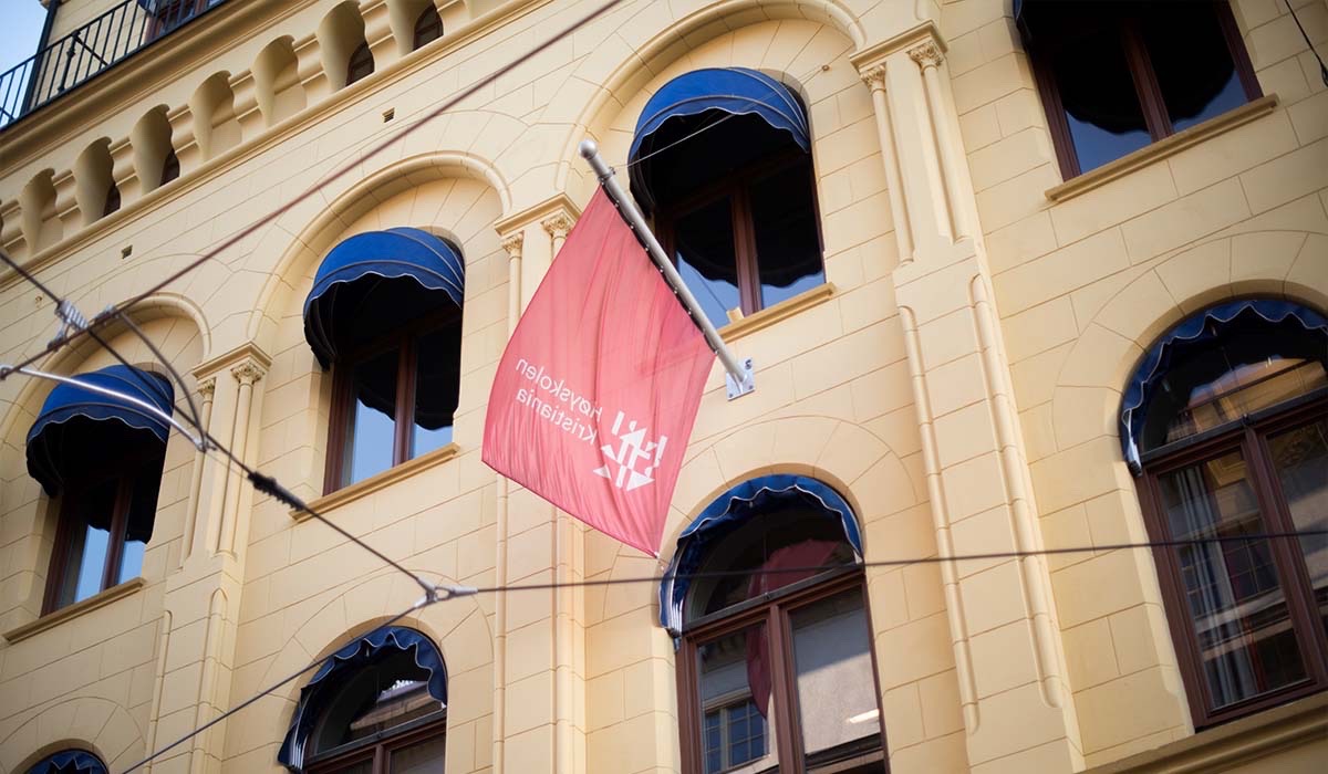 Fasaden til Høyskolen Kristianias bygg i Kvadraturen er fotografert. Et rødt flagg med Kristianias logo vaier i vinden.