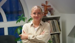 Eline Langøy Brattsi har blondt hår i en hestehale og briller. Hun har på seg en kremhvit skjorte og holder armene i kors.