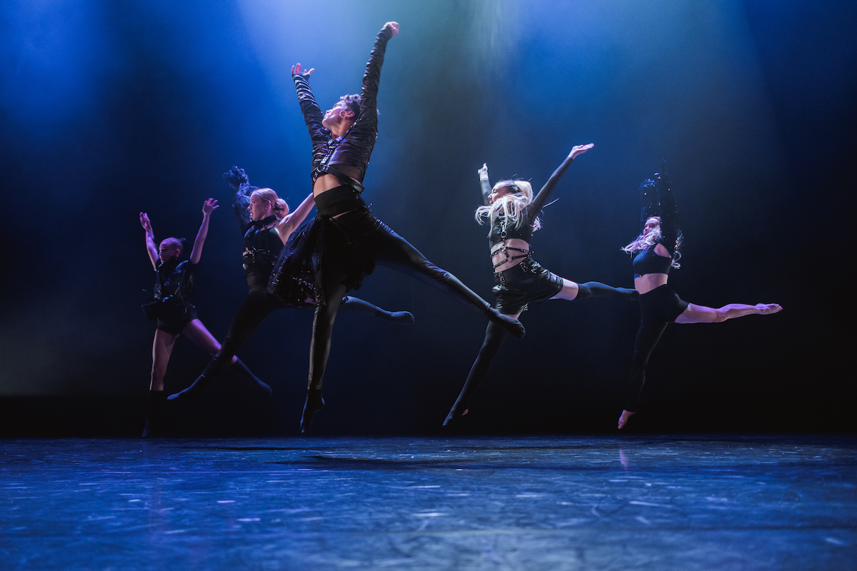 Fem dansere hopper synkront på en scene.