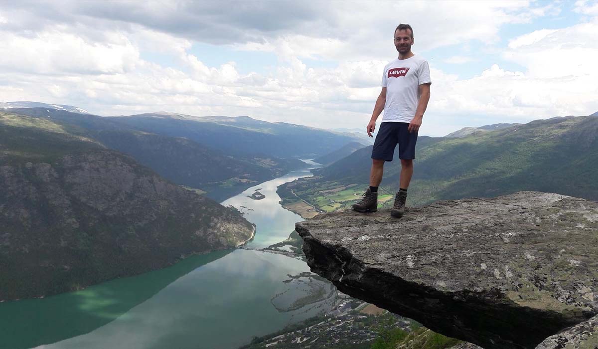  Prosessingeniør Kim Nilsen står på kanten av en klippe mens han ser rett på kamera. Han har på seg svart shorts og hvit t-skjorte.