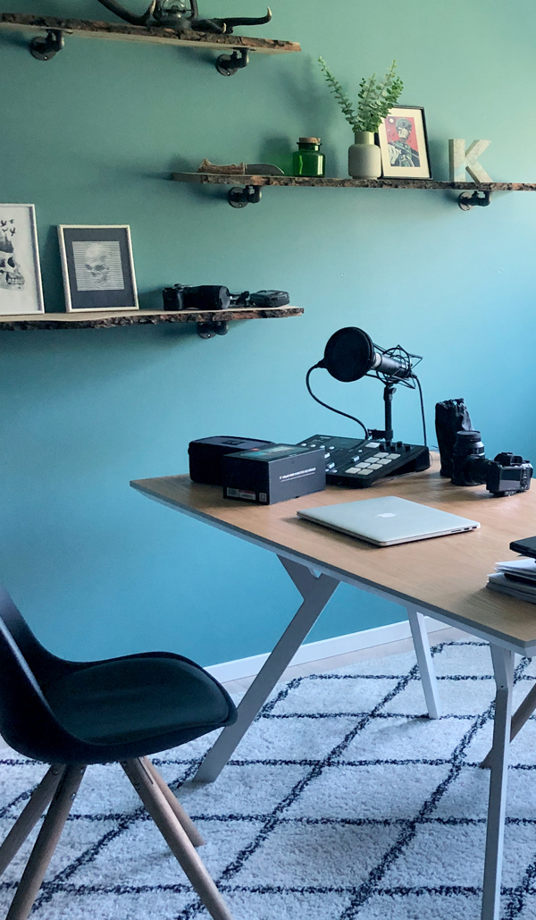 Tidligere student ved Fagskolen Kristiania, Kristine Blesvik Andersen driver design-byrået KastleBlack. På bildet ser man hjemmekontoret hennes, med tre vegghengte hyller med pynt på, en pult med Mac og fotoutstyr og en svart stol.