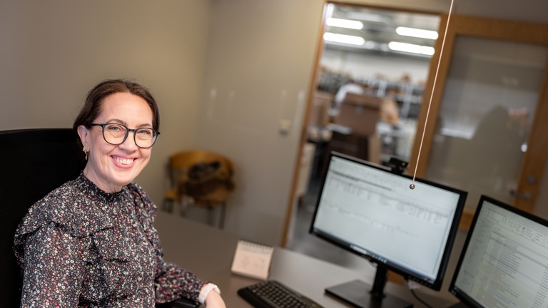 Person smiler inn i kamera og sitter på et kontor foran en PC