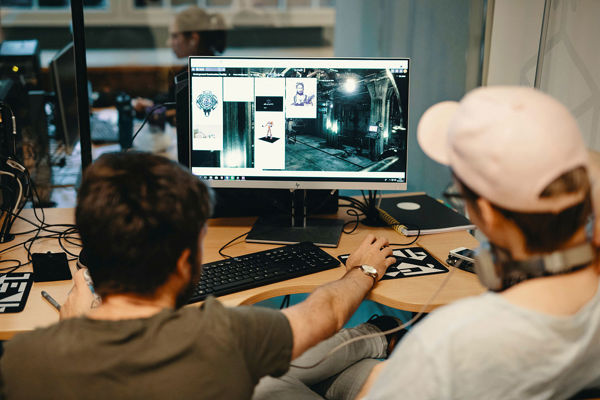 To gutter sitter med ryggen til og ser på en dataskjerm, hvor de animerer et dataspill. 