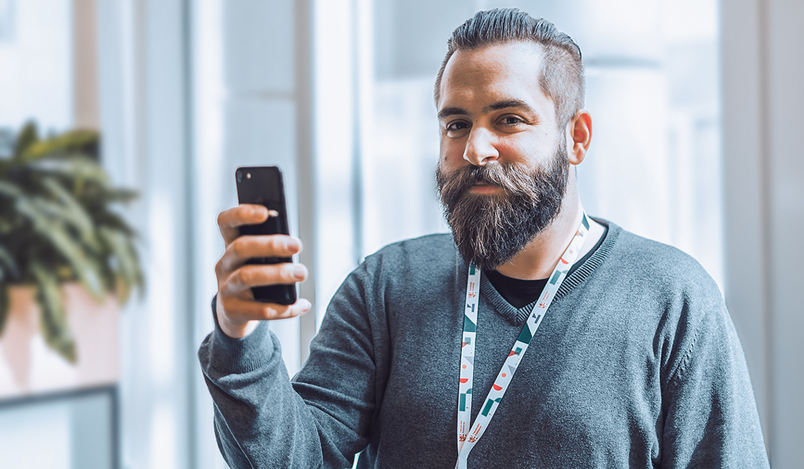 Dennis står med mobiltelefonen i hånda og smiler til kamera.