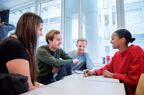 Fire studenter som sitter rundt en pult og diskuterer noe spennende
