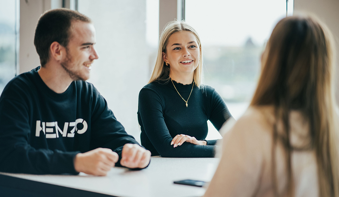 Tre studenter sitter sammen ved et bord.