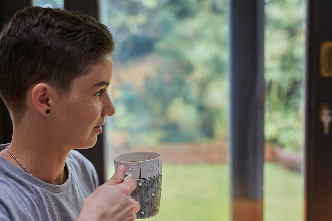 Kvinne med kaffekopp ser ut av vinduet