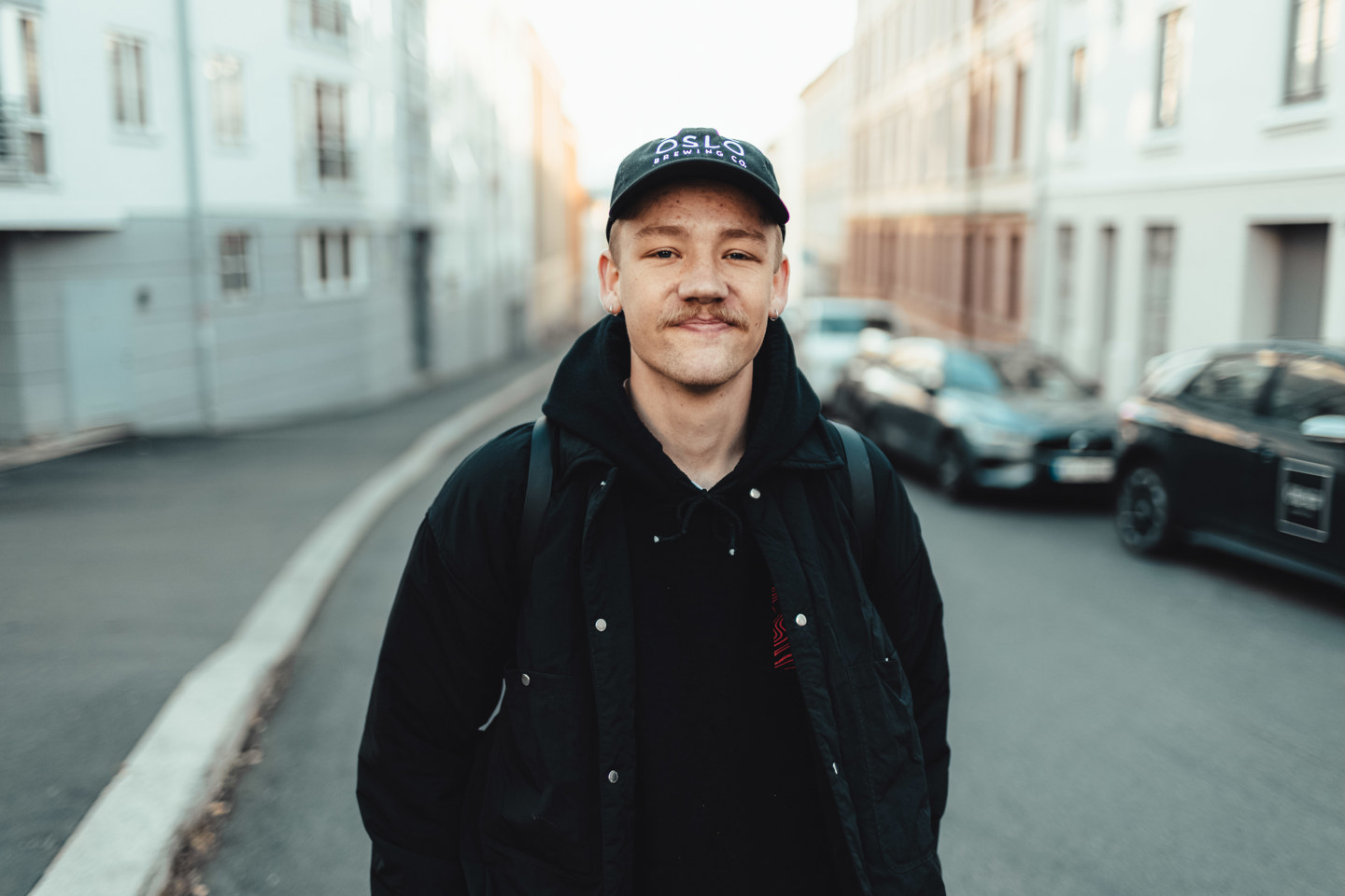 Bilde av mann i sorte høstklær og caps som står i en urban gate.