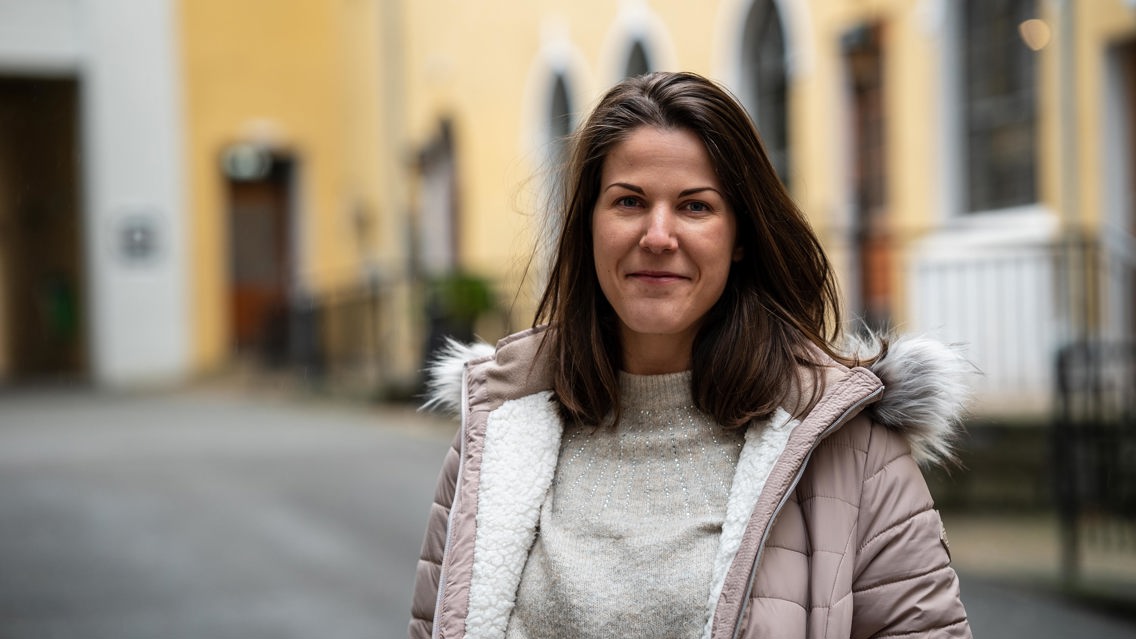 Foto av Ingvild utenfor campus Hansaparken i Bergen. Hun har mørkt hår og har på seg en lys vinterjakke. 