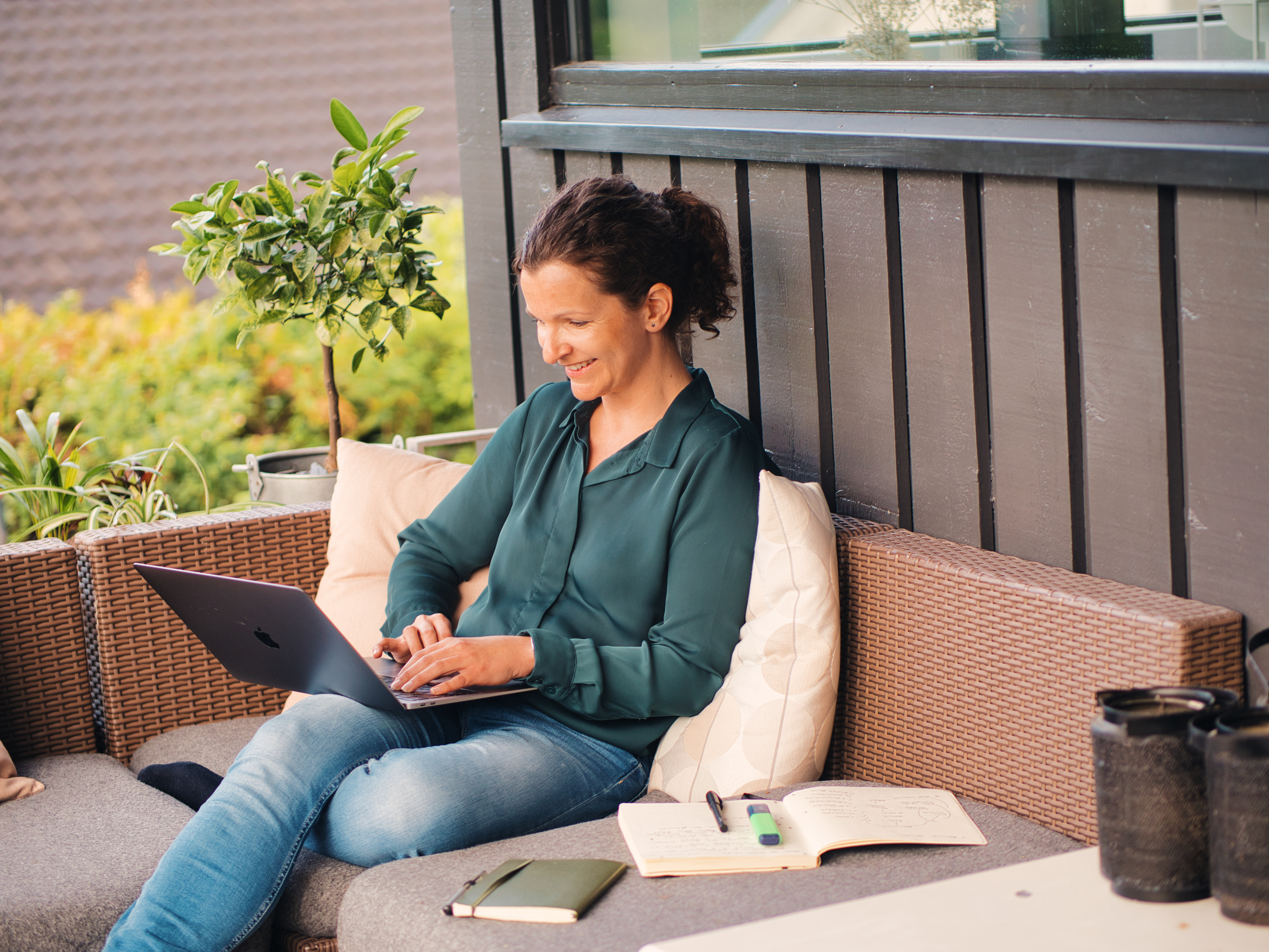Foto av en kvinne som sitter på terrassen med laptopen sin.